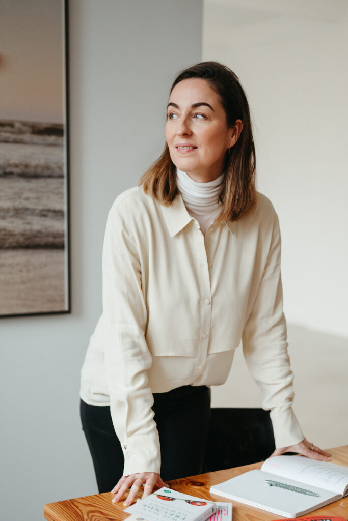 Henrike Redecker steht am Tisch und schaut zur Seite. Vor ihr liegen Bücher und ein Notizbuch.