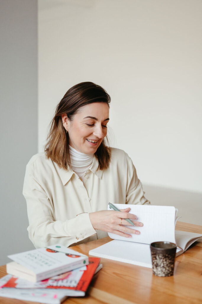 Henrike Redecker blättert in einem Notizbuch am Holztisch, daneben liegen Bücher und eine Tasse.