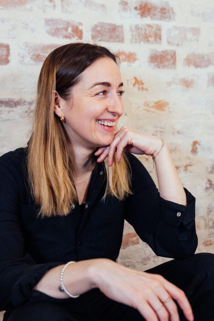 Henrike Redecker lacht im Profil vor einer Backsteinwand.